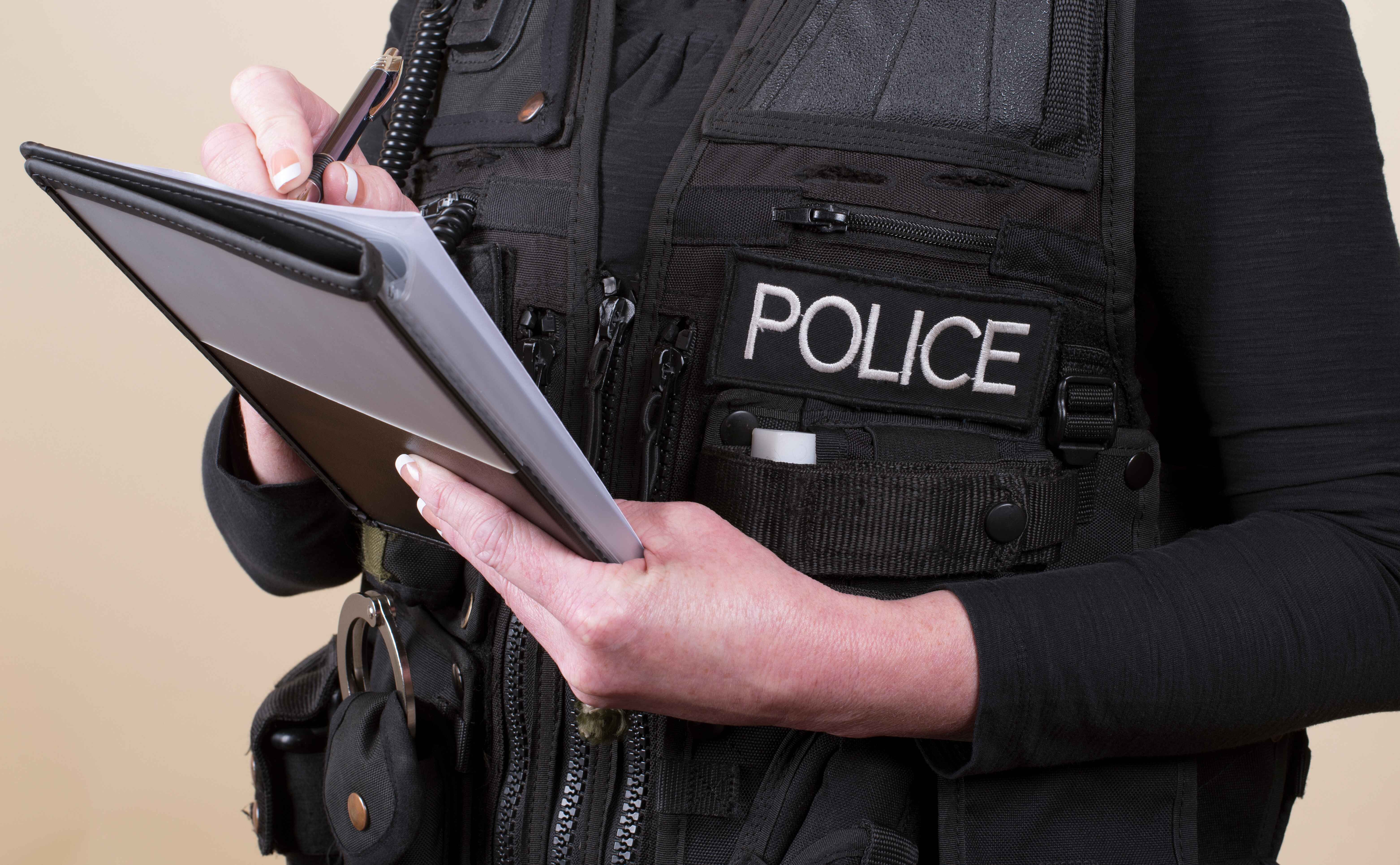 Person in a police vest writing in a notebook.