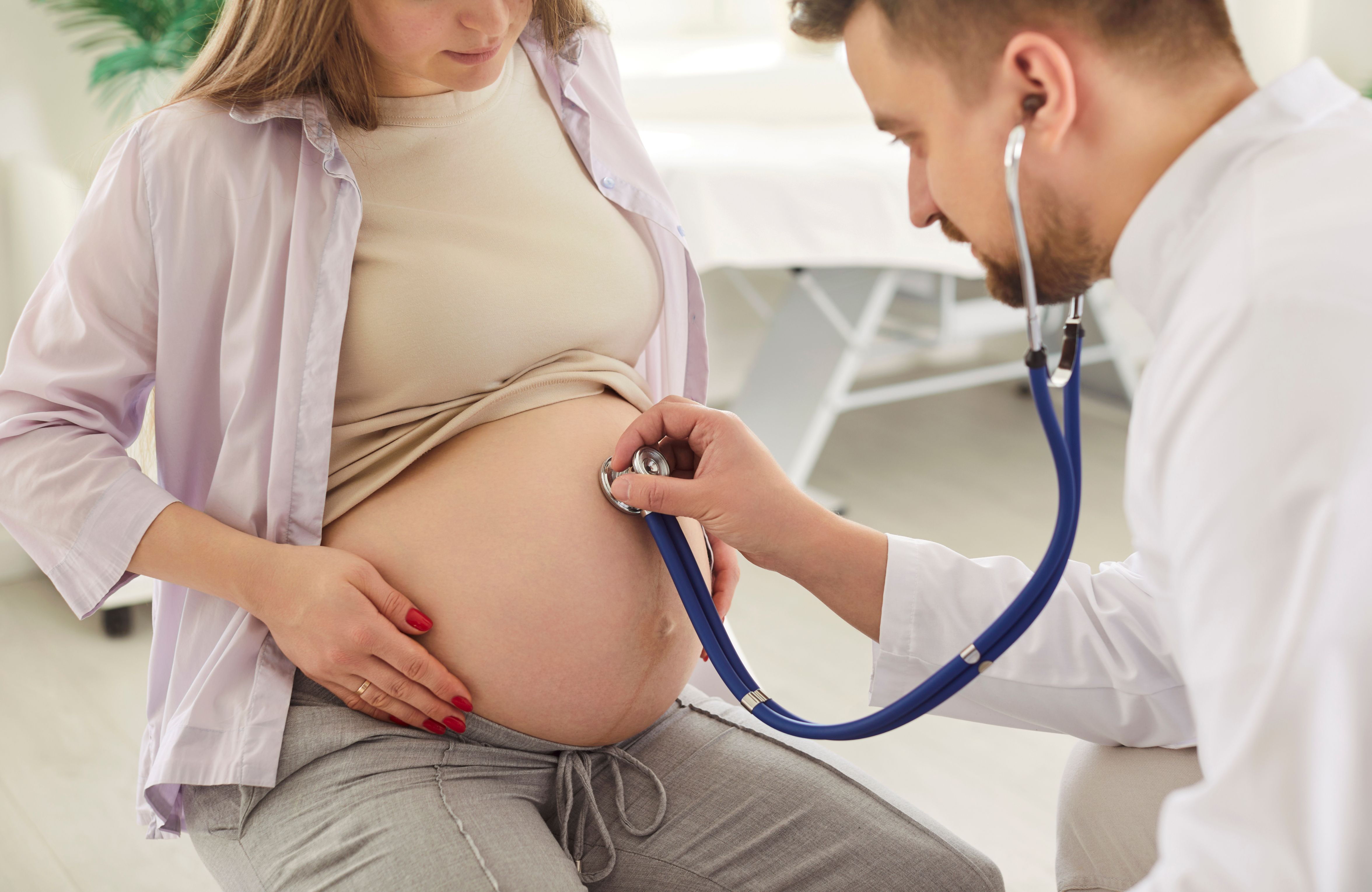 A heavily pregnant person is examined by a doctor using a stethoscope on her stomach