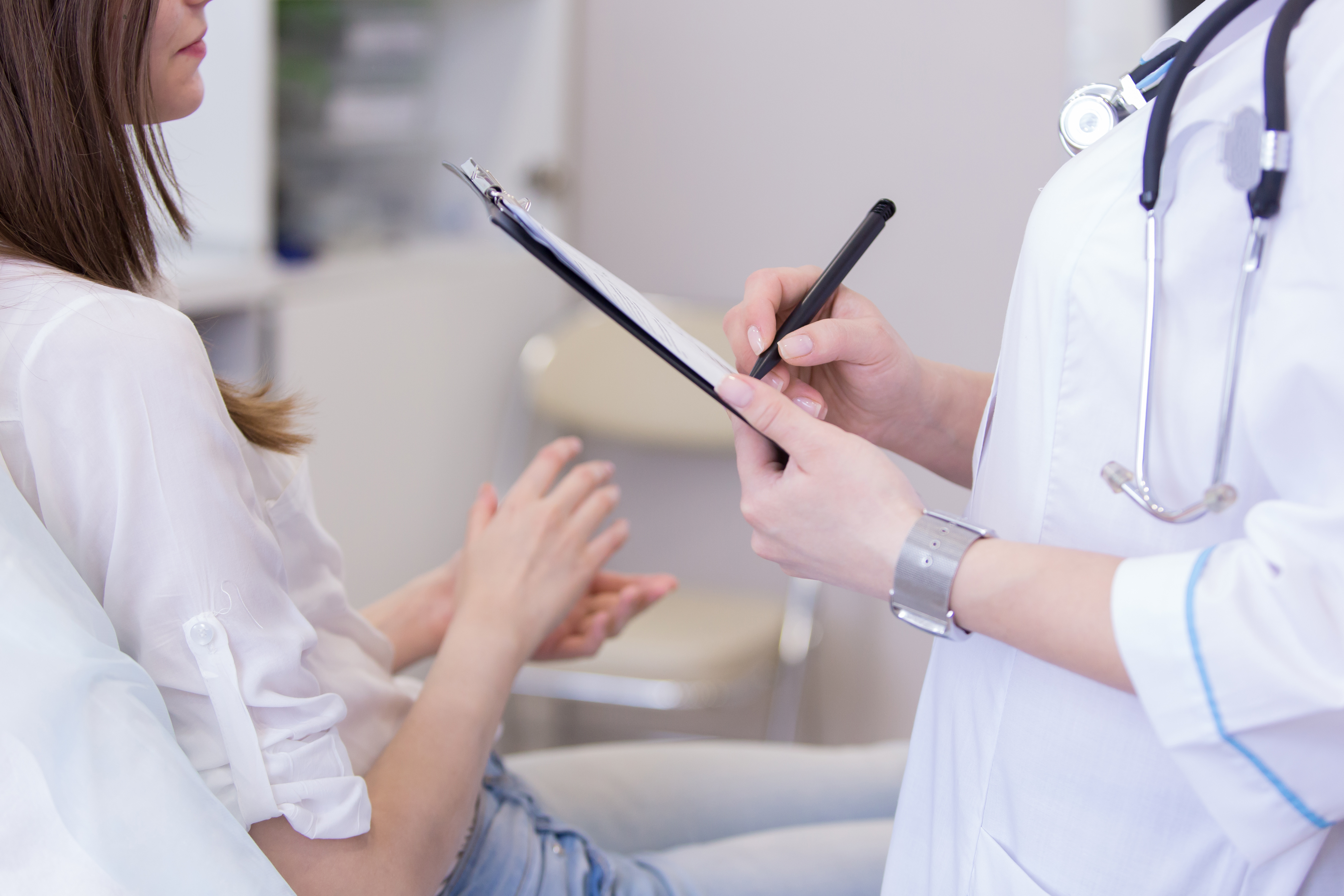 Young woman speaks with a doctor holding a clipboard 