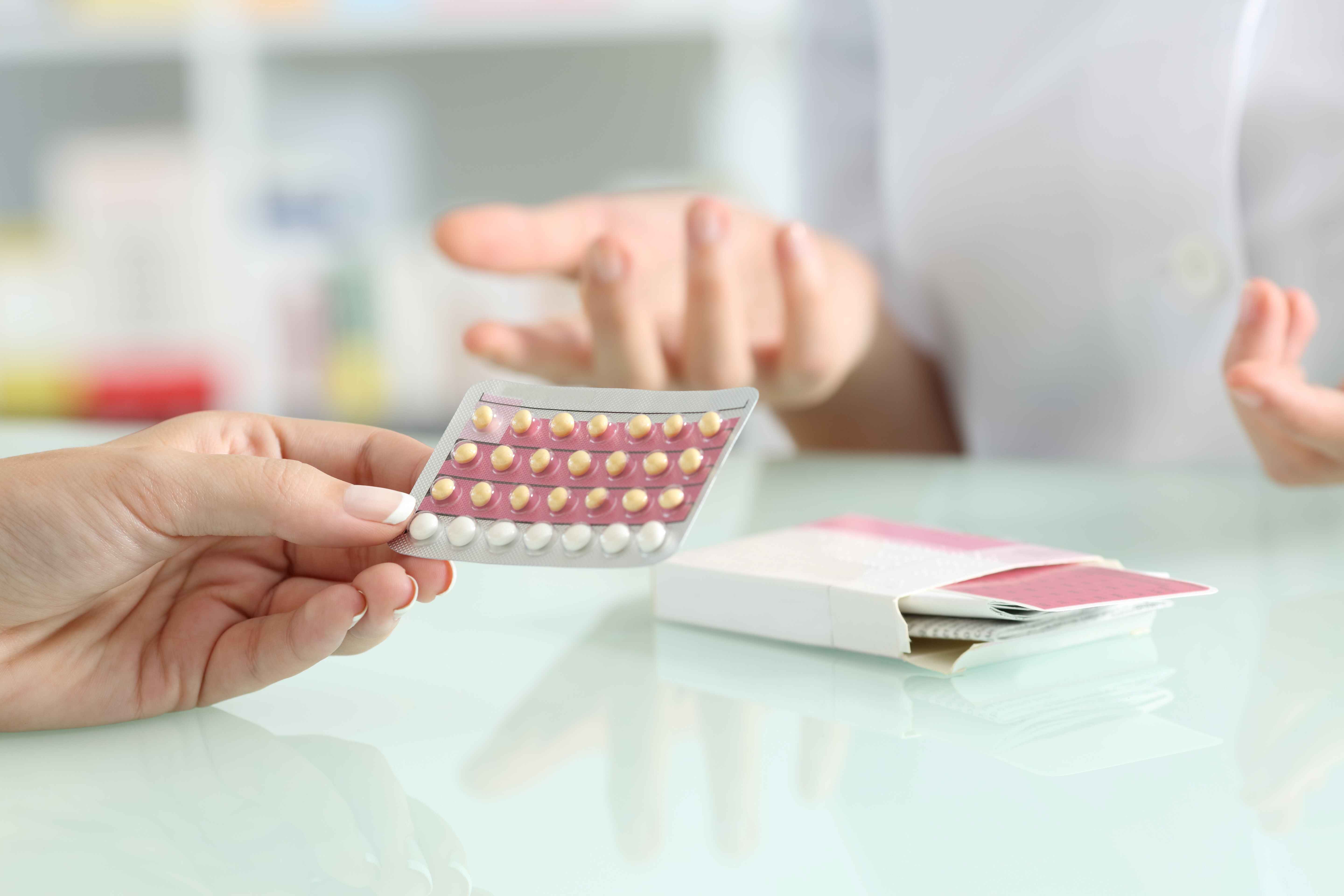 Close-up of a hand holding a blister pack of birth control pills in a consultation setting.