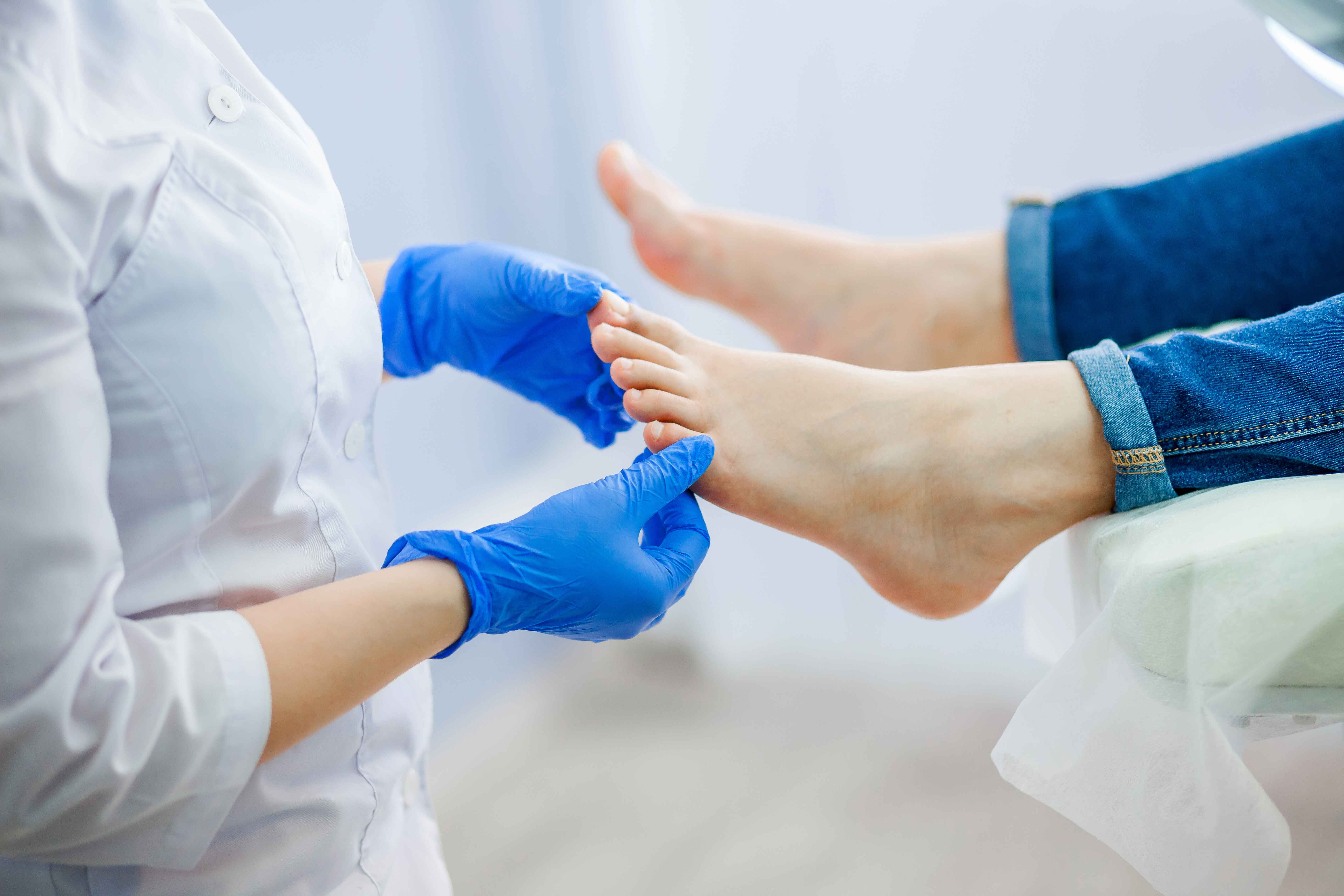 A gloved person examines another's foot in a medical setting.