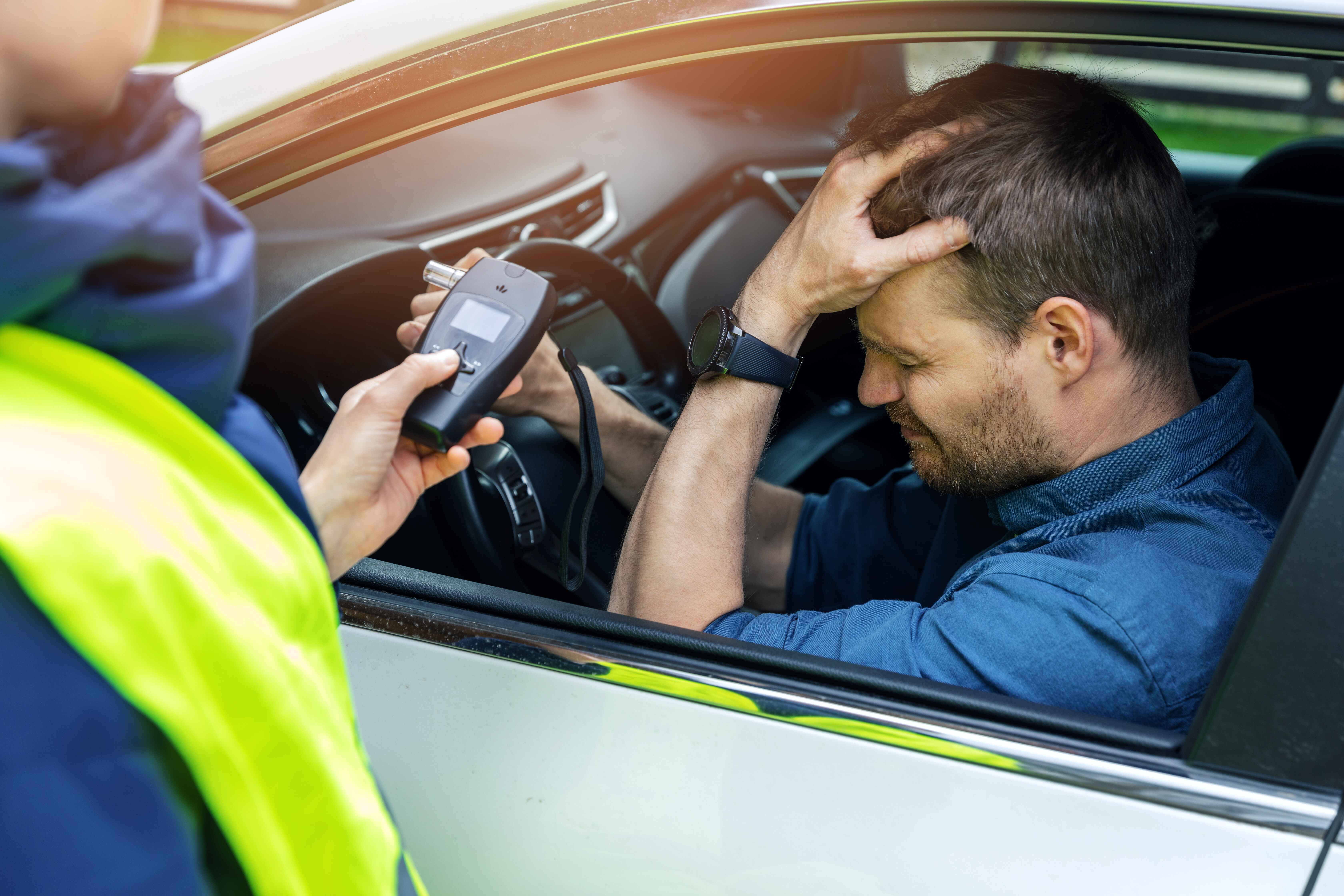 A man sitting in a car being offered a breathalyzer by a police officer.