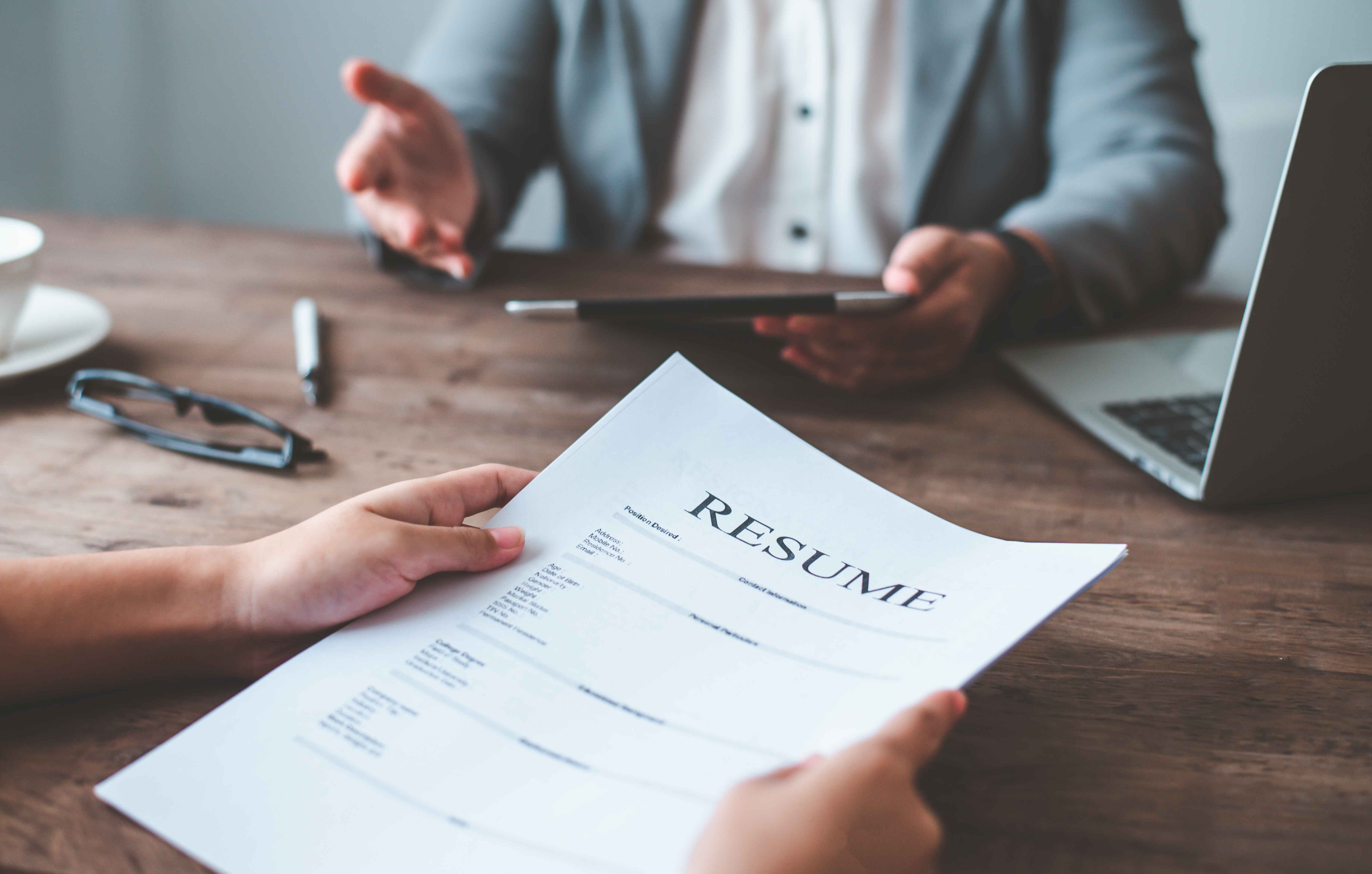 Person holding a resume during a job interview, with another person in a gray suit across the table.