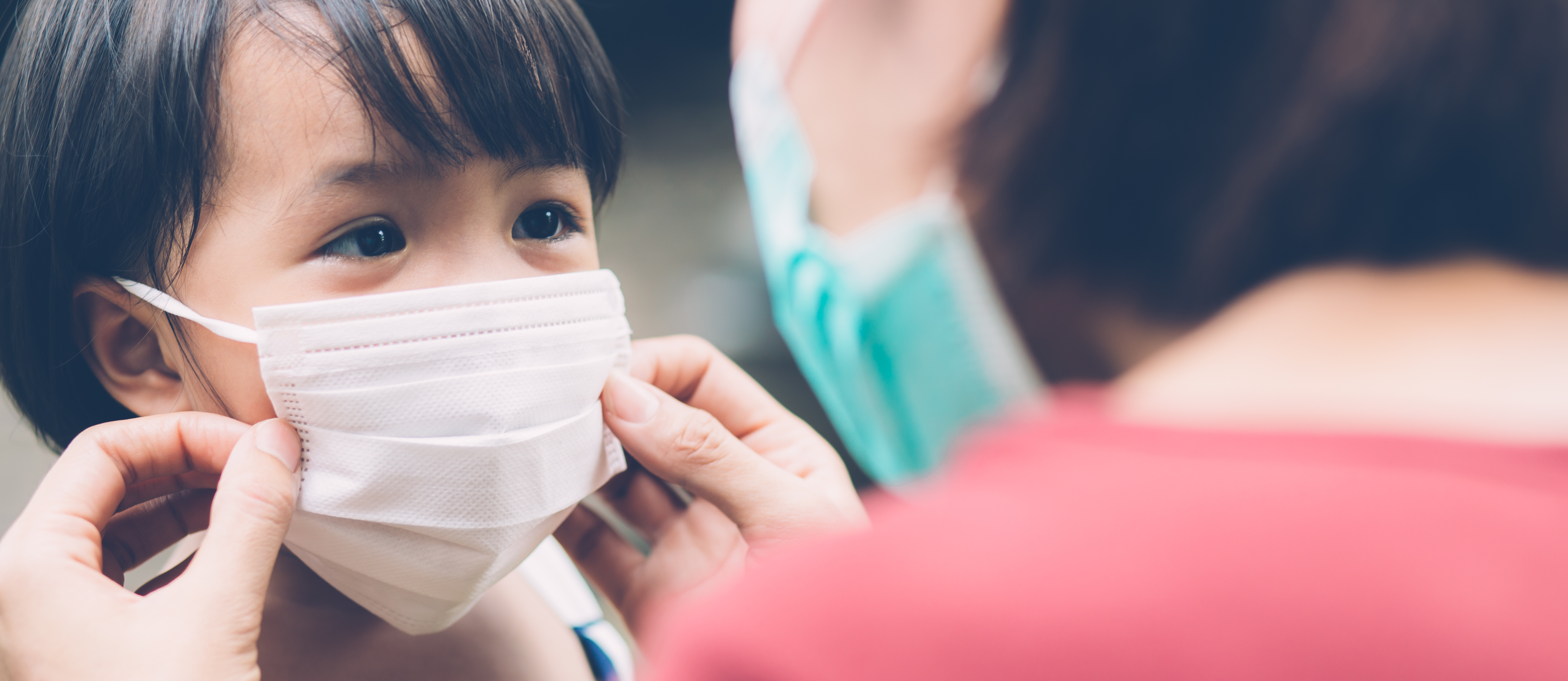 A child wearing a face mask being adjusted by an adult.