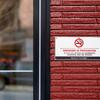 Sign prohibiting smoking mounted on a red brick wall next to a glass door.