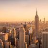 Panoramic view of New York City skyline at sunset with skyscrapers and the Hudson River in the background.