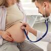 A heavily pregnant person is examined by a doctor using a stethoscope on her stomach