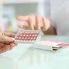 Close-up of a hand holding a blister pack of birth control pills in a consultation setting.