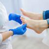 A gloved person examines another's foot in a medical setting.