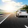 A white SUV driving on a sunny highway with mountain scenery.
