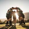 A group of soccer athletes huddled together on a field with the sun setting behind them.