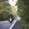 A motorcyclist rides through a forested road, wearing a black jacket and helmet.