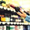 Person holding a bottle of red wine in a store aisle.