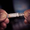 Hands holding a glass vial labeled "METHADONE."