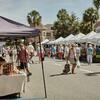 Outdoor market with tents, people shopping, and produce on display.