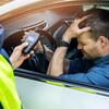 A man sitting in a car being offered a breathalyzer by a police officer.