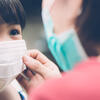 A child wearing a face mask being adjusted by an adult.
