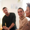 Four people speaking to each other sitting in a circle, a white woman with blonde hair, a white man with brown hair, a white woman with brown hair, and a black woman with curly brown hair