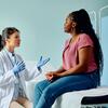 A healthcare professional in a white coat consults with a patient on an examination table near an ultrasound machine.
