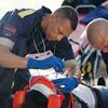 Two paramedics treat a patient with a bandaged head and oxygen mask on the ground.