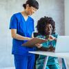 Two healthcare professionals in scrubs reviewing information on a laptop.