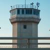 Two guards standing on a platform in front of a concrete watchtower.
