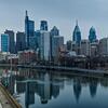 Philadelphia skyline with skyscrapers reflected in a river and highway traffic in the foreground.