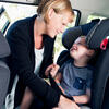 Adult helping a child in a car seat inside a vehicle.