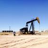 An oil pumpjack in a dry landscape with oil tanks and a clear blue sky.