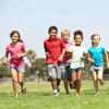 Six children running on grass in a park under a clear sky.