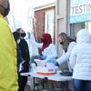 Outdoor COVID-19 testing site with people in line and healthcare workers administering tests.