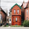A red brick house with green roof accents and a white door, flanked by similar buildings.