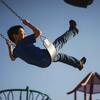 Boy swinging against a clear blue sky at a playground.