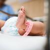 Close-up of a newborn's feet with a pink hospital ID band in a crib.